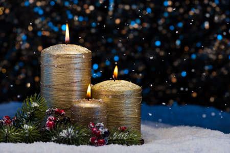 Three Golden Candles in snow with snowfallの写真素材