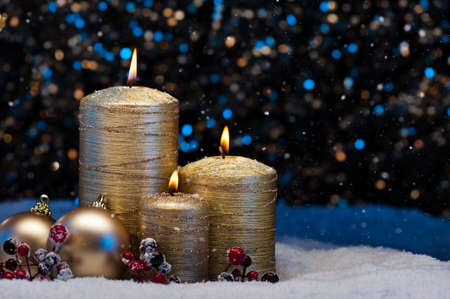 Three Golden Candles in snow with snowfallの写真素材