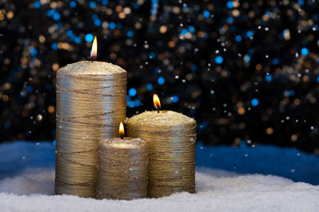 Three Golden Candles in snow with snowfallの写真素材