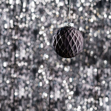 Black Christmas tree bauble over silver glitter backgroundの写真素材