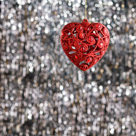 Red heart christmas ornament over silver glitter backgroundの写真素材
