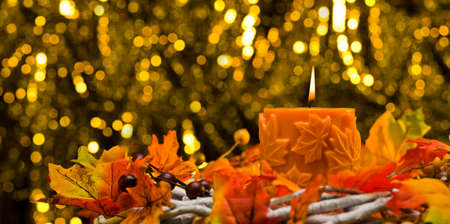 Orange candle in autumn Christmas setting in front of a golden backgroundの写真素材