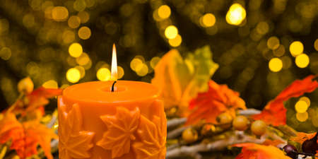 Orange candle in autumn Christmas setting in front of a golden backgroundの写真素材
