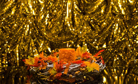 Orange candle in autumn Christmas setting in front of a golden backgroundの写真素材