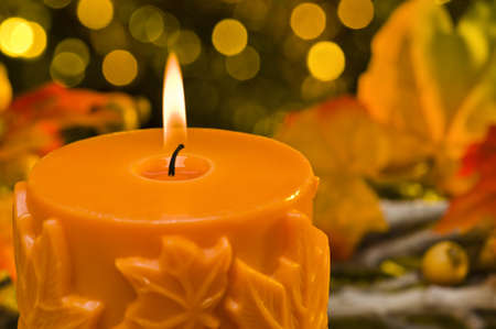 Orange candle in autumn Christmas setting in front of a golden backgroundの写真素材