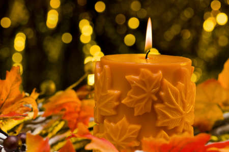Orange candle in autumn Christmas setting in front of a golden backgroundの写真素材