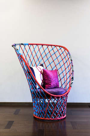 Red purple blue tone wicker chair in front of a plain wallの写真素材