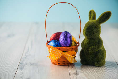 Easter eggs in a basket with a bunny on a white tableの写真素材