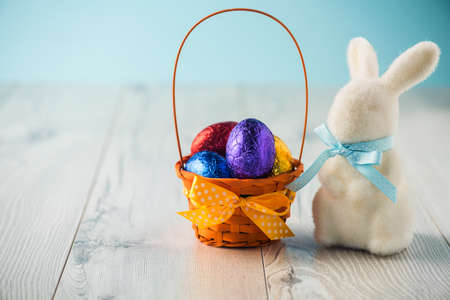 Easter eggs in a basket with a bunny on a white tableの写真素材