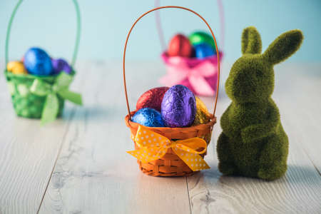 Easter eggs in a basket with a bunny on a white tableの写真素材