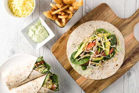 shredded barbecued chicken wraps with carrot, cheese, avocado and spinach. With French fries on the side.の写真素材