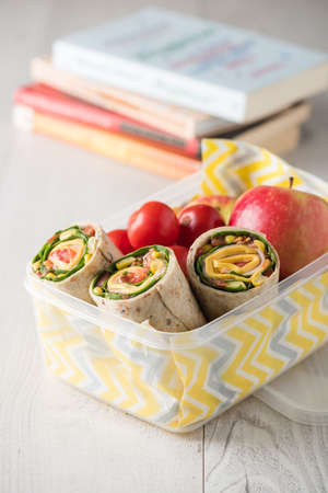 Ham and cheese wraps in lunch box with apple and tomatoesの写真素材