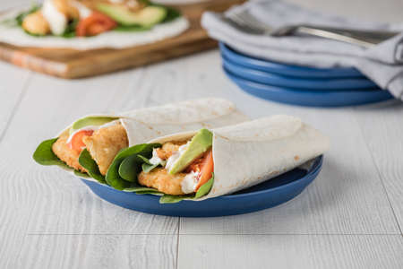 Fish finger wraps with avocado and tomato serves on blue plateの写真素材
