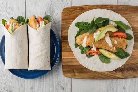 Fish finger wraps with avocado and tomato serves on wooden cheese platterの写真素材