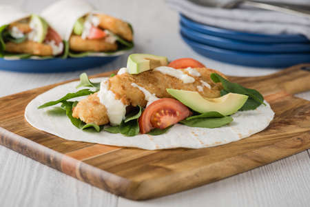 Fish finger wraps with avocado and tomato serves on wooden cheese platterの写真素材