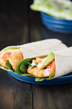 Crumbed fish fillet burrito with avocado and tomato on rustic backgroundの写真素材