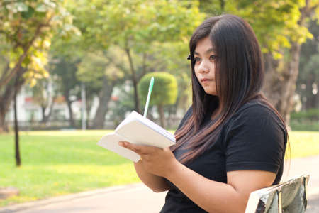 Woman sitting in a park thinking what to write in books.
の写真素材