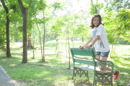 Woman standing on a stool. In the park with trees and greenery.の写真素材
