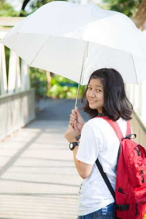 Young woman holding a white umbrella. In the middle of a bridge over the river in the park.の写真素材