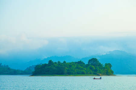 Fishing lake and small island fishing boats fishing in the early morning fog covered the mountain.の写真素材
