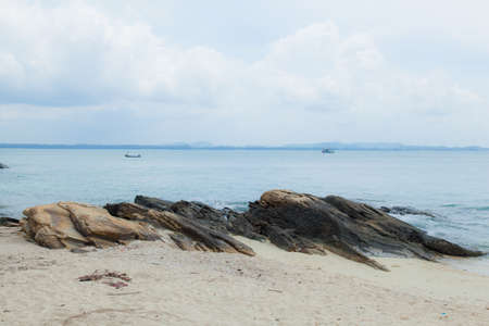 Large rocks on a sandy beach with small fishing boats in the sea.の写真素材