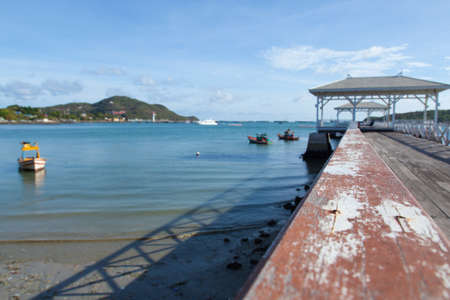 Wooden bridge stretching into the sea. Small boats moored nearby.の写真素材