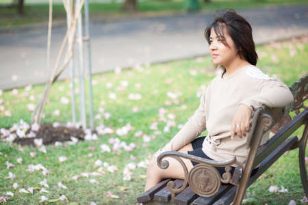 Woman sitting on bench Vacant look forward Blossoms in the Yard