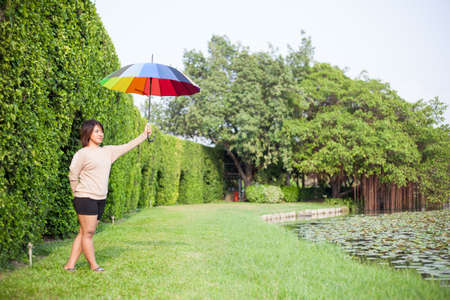 Asian woman holding an umbrella in the park. Stood on the lawn beside a tree.の写真素材
