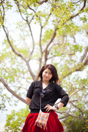 Asian women black shirt standing under a tree. Happy smiling relaxing in the park.の写真素材