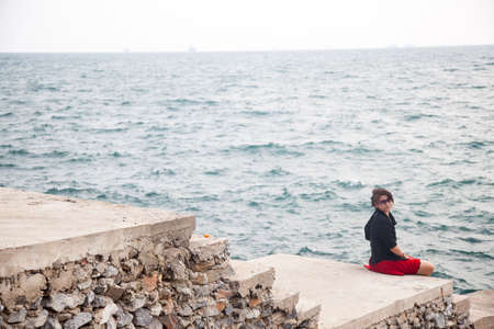 Asian women black shirt. Sitting on the sidewalk. A bridge near the oceanの写真素材