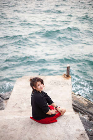 Asian women black shirt. Sitting on the sidewalk. A bridge near the oceanの写真素材