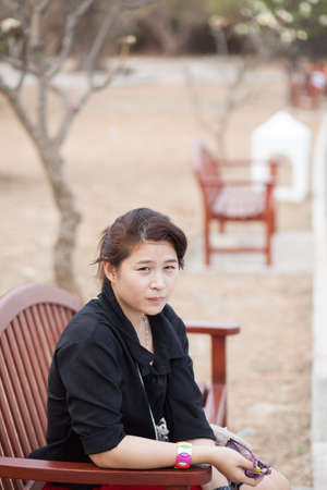 Asian women black shirt. Sitting on wooden bench. Adjacent to the corridor of the park.の写真素材