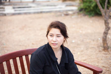 Asian women black shirt. Sitting on wooden bench. Adjacent to the corridor of the park.の写真素材