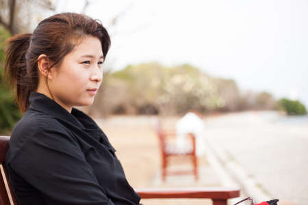 Asian women black shirt. Sitting on wooden bench. Adjacent to the corridor of the park.