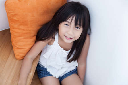 Child girl sitting on the ladder. child with long hair orange pillow in the background.の写真素材