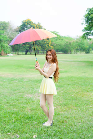 Woman with umbrella standing on the lawn. In the park during the day, the sun is strongest.の写真素材