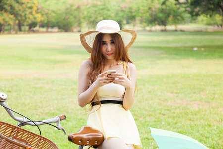 Woman play smart phone.on bike in lawn.in park.の写真素材