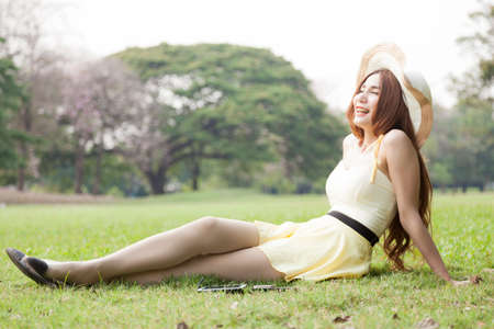 Relaxing on the lawn. Woman wearing hat sitting and relaxing on the grass in the park.の写真素材