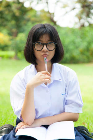 Schoolgirl is sitting homework. On the grass in the park. Problems with homeworkの写真素材