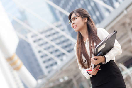 Happy asian businesswoman hold paper and document file.smile and stand on sidewalk.