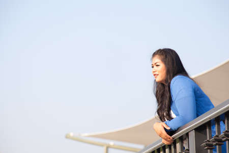 Woman standing at the balcony. Looking ahead and smiling happily.の写真素材