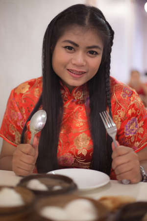 Woman wearing red cheongsams holding a spoon and fork. In front of a restaurantの写真素材