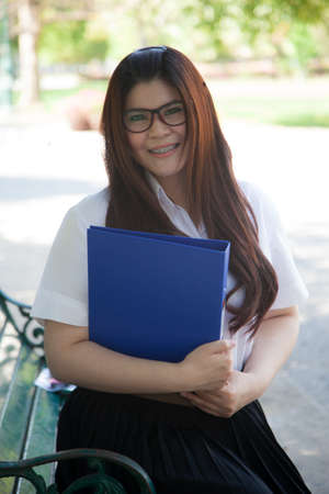 Student wearing glasses, holding a document. Sitting on a bench in the park.の写真素材