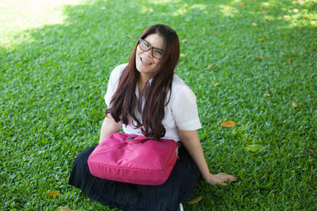 Female student sitting on the lawn. Pink bag was placed on it.の写真素材