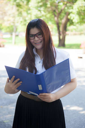 Student holding a blue documents. Student wearing glasses, standing smiling and holding a file exists.の写真素材