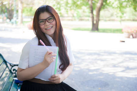 Student wearing glasses, holding a document. Sitting on a bench in the park.の写真素材