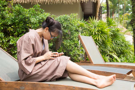 Woman couch And play smart phones. On wood bed beside the pool.の写真素材