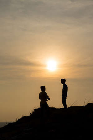 Silhouettes of people standing on the mountain. In the evening, the sun was falling.の写真素材