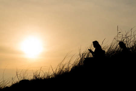 Silhouettes of person. Sits on the slopes of the mountains in the evening sun falls.の写真素材