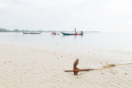 Anchor resting on the beach. Small fishing boat moored at sea.の写真素材